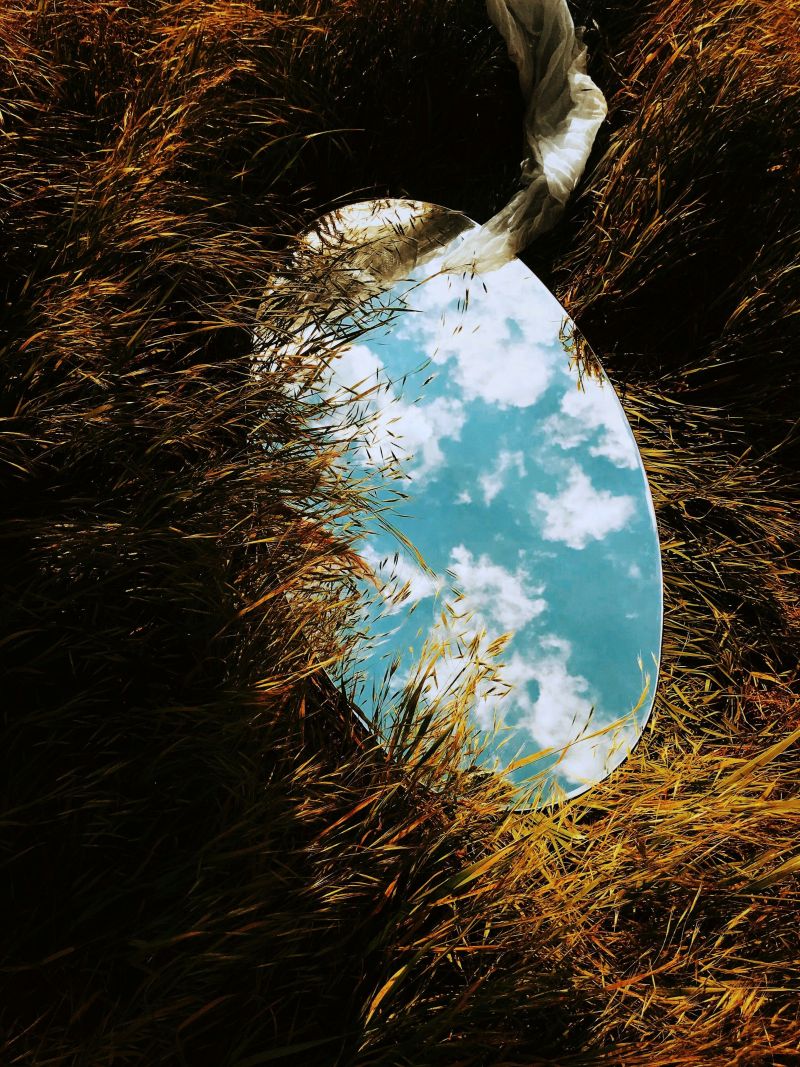 mirror in dry grass showing a beautiful sky